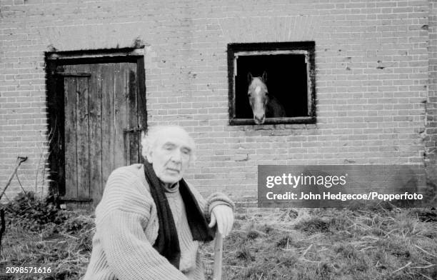 English poet George Barker seated on a red chair in front of farm buildings in Norfolk, England in 1966. George Barker and his family have recently...