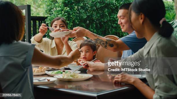 young asian family eating chinese food and having fun sitting at dining table at backyard outside home. multi-generation family enjoying spending together. - chinese eating backyard stock pictures, royalty-free photos & images