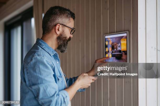 man adjusting household functions, lighting, security cameras, door locks and thermostat or heating settings in the smart home system. - green building stock pictures, royalty-free photos & images