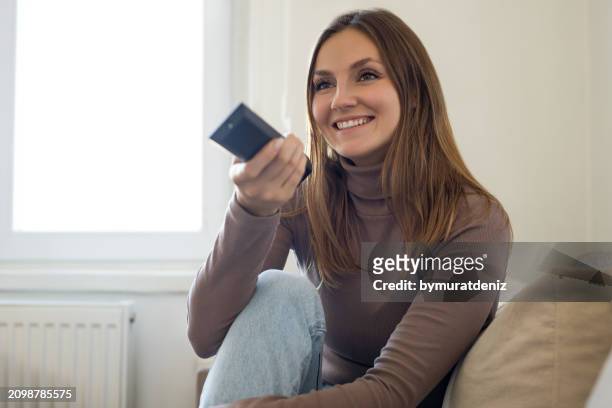 woman sitting on the sofa watching tv - film screening room stock pictures, royalty-free photos & images