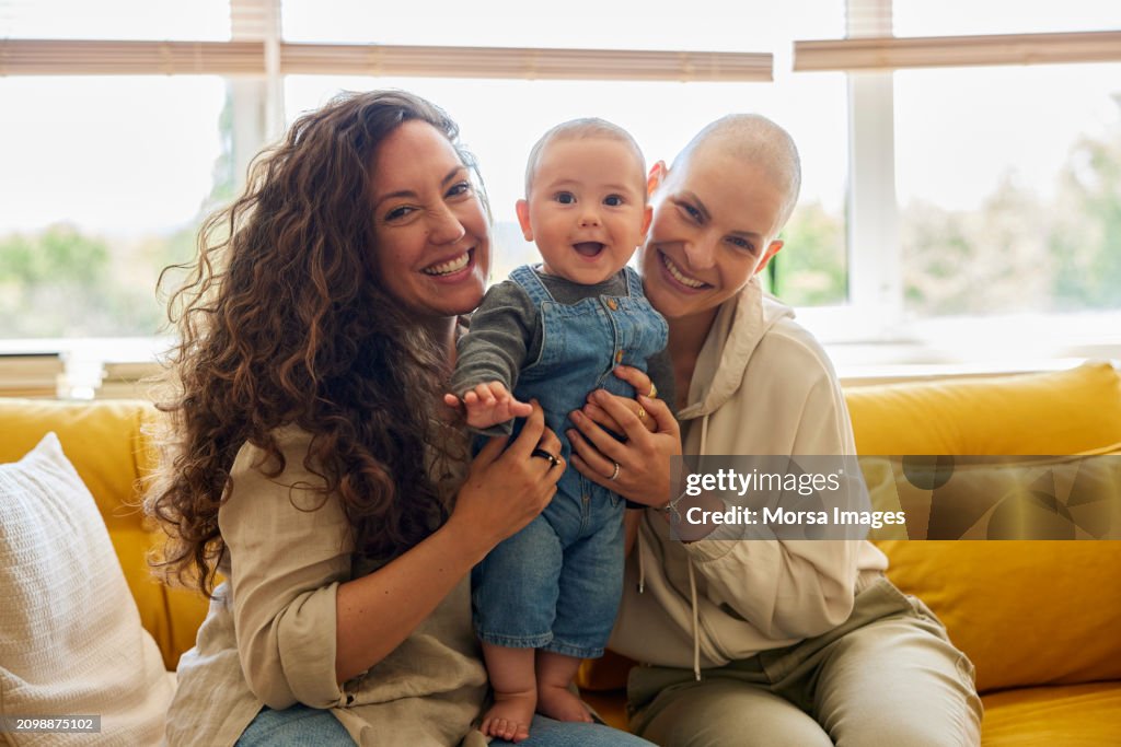 Friends playing with toddler on sofa at home