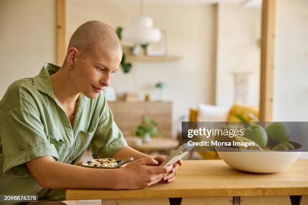 female cancer patient messaging through phone while having breakfast - alopecia stockfoto's en -beelden