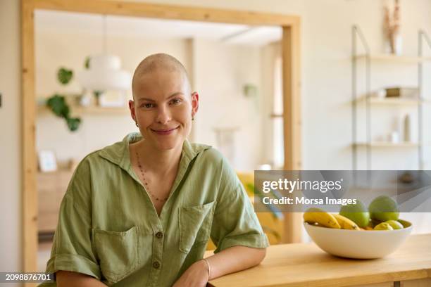 smiling female cancer patient sitting by fruit at table in kitchen - alopecia fotografías e imágenes de stock