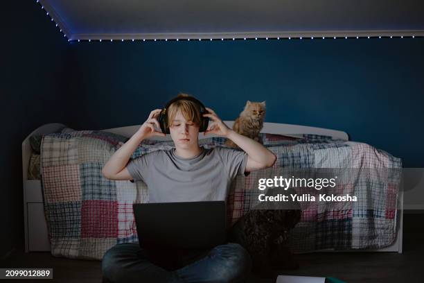 teen boy at home and playing laptop or reading online and listening to music with wireless headphones - kurve abflachen stock-fotos und bilder