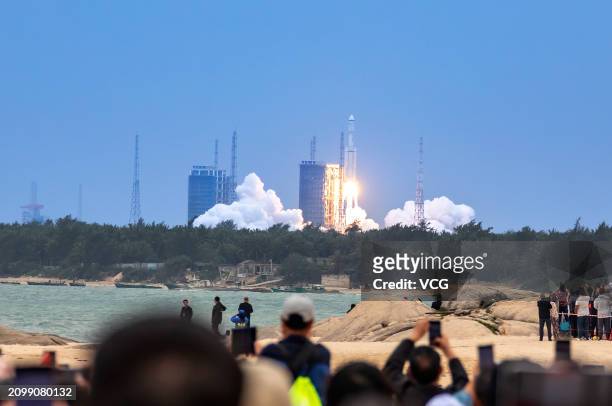 Spectators watch as the Long March-8 Y3 carrier rocket carrying the relay satellite Queqiao-2 blasts off from the Wenchang Spacecraft Launch Site on...