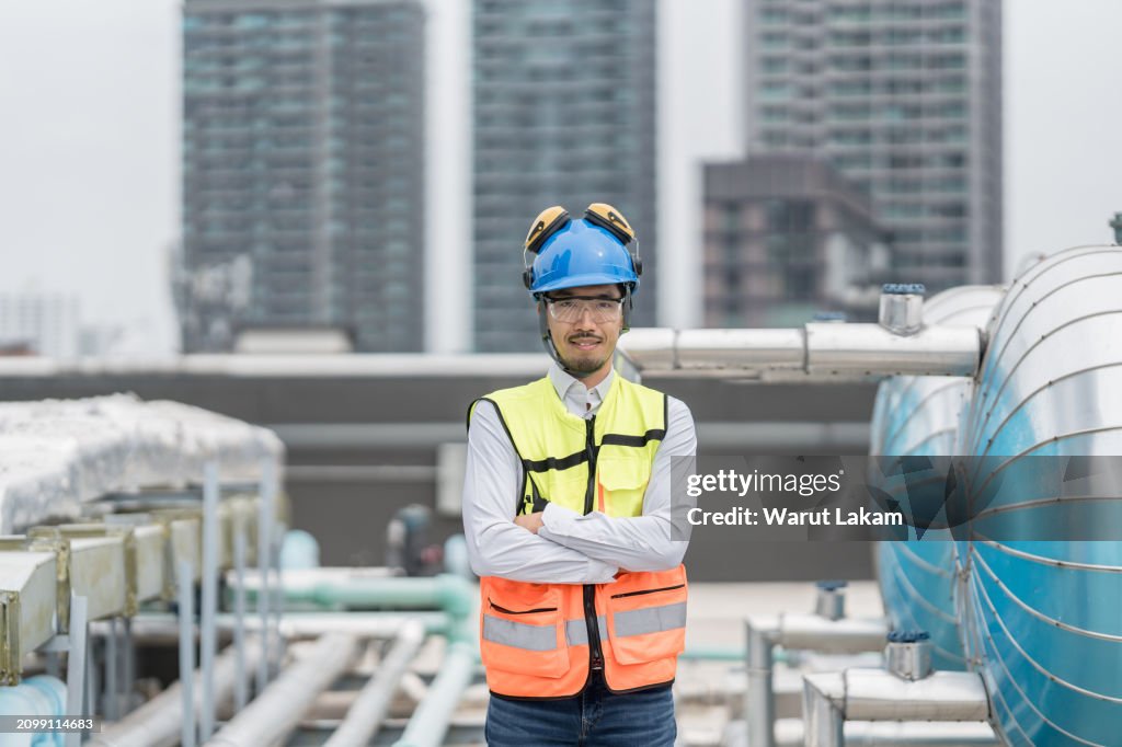 Confident Engineer Stands with Industrial Tanks, Symbolizing Technological Oversight and Safety.