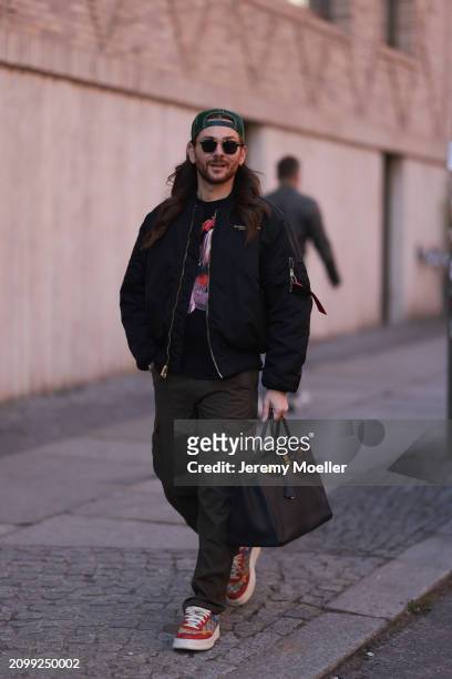 Riccardo Simonetti seen wearing Gucci gold / black sunglasses, Stetson green logo cap, Alpha Industries black oversized bomber jacket, black with...