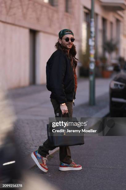 Riccardo Simonetti seen wearing Gucci gold / black sunglasses, Stetson green logo cap, Alpha Industries black oversized bomber jacket, Carhartt dark...