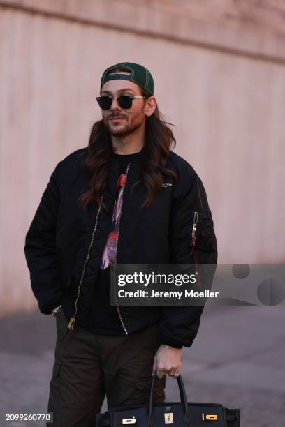 Riccardo Simonetti seen wearing Gucci gold / black sunglasses, Stetson green logo cap, Alpha Industries black oversized bomber jacket, black with...