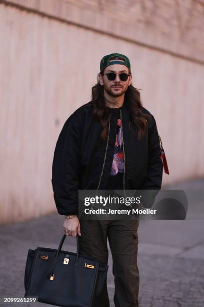 Riccardo Simonetti seen wearing Gucci gold / black sunglasses, Stetson green logo cap, Alpha Industries black oversized bomber jacket, black with...