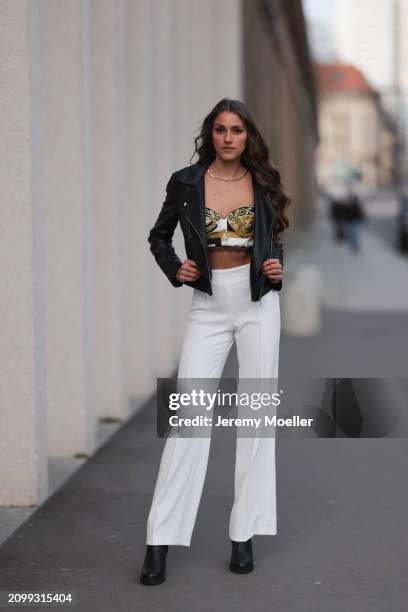 Michelle Golke seen wearing gold necklace, black / white / yellow pattern crop top, black leather biker jacket, white wide leg pants and black...