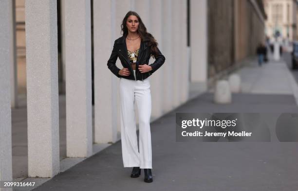 Michelle Golke seen wearing gold necklace, black / white / yellow pattern crop top, black leather biker jacket, white wide leg pants and black...