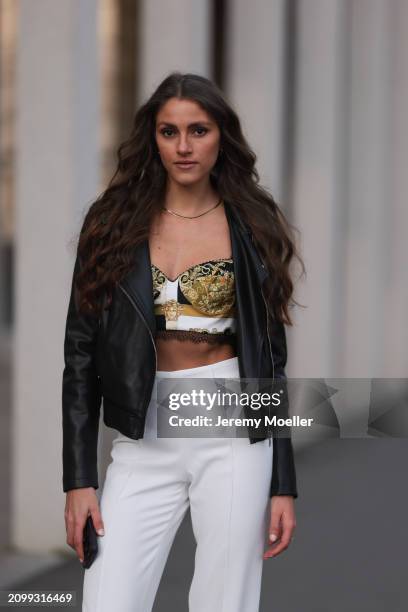 Michelle Golke seen wearing gold necklace, black / white / yellow pattern crop top, black leather biker jacket and white fabric wide leg pants, on...