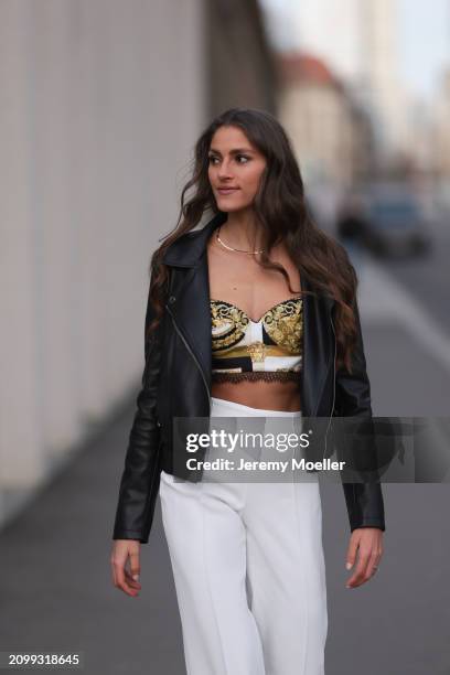 Michelle Golke seen wearing gold necklace, black / white / yellow pattern crop top, black leather biker jacket and white fabric wide leg pants, on...