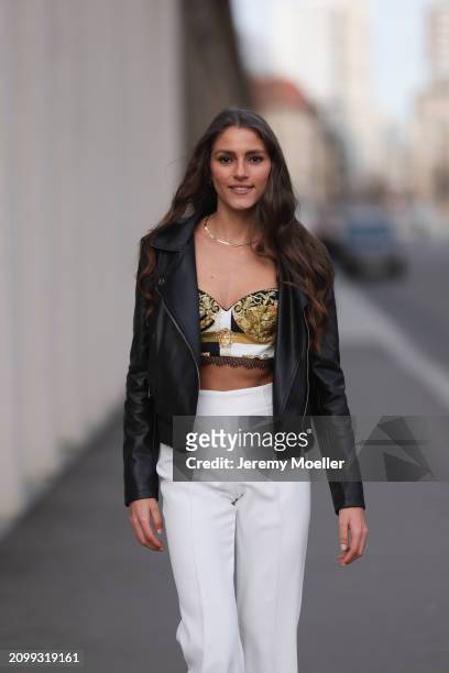 Michelle Golke seen wearing gold necklace, black / white / yellow pattern crop top, black leather biker jacket and white fabric wide leg pants, on...