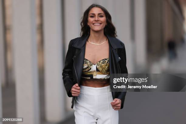 Michelle Golke seen wearing gold necklace, black / white / yellow pattern crop top, black leather biker jacket and white fabric wide leg pants, on...