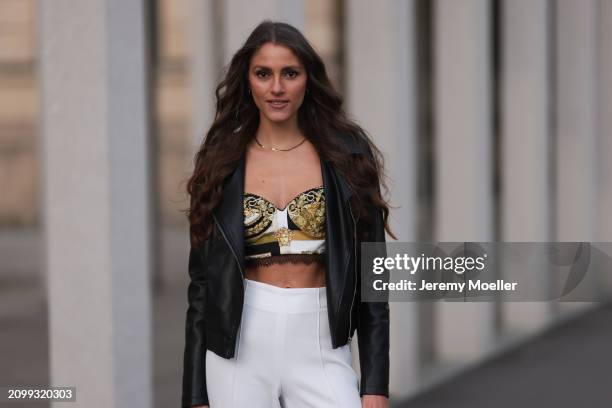 Michelle Golke seen wearing gold necklace, black / white / yellow pattern crop top, black leather biker jacket and white fabric wide leg pants, on...