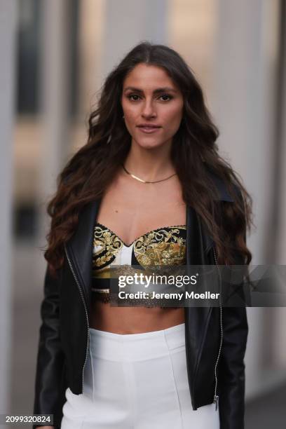 Michelle Golke seen wearing gold necklace, black / white / yellow pattern crop top, black leather biker jacket and white fabric wide leg pants, on...