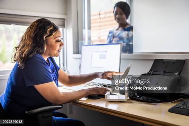 female nurse accepting payment from patient at reception desk in doctor's office - reportage hospital stock pictures, royalty-free photos & images