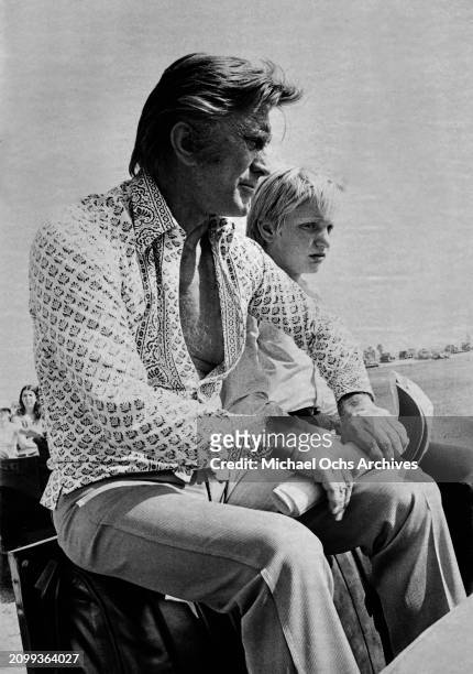 American actor and film director Kirk Douglas, wearing a patterned shirt, sits beside his son, Eric, circa 1975. The image was shot for Rona...