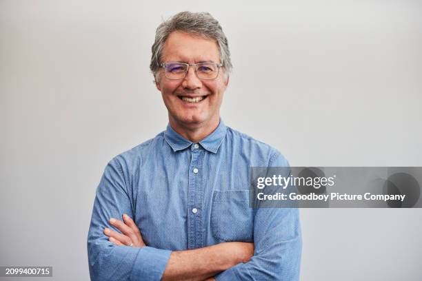 reifer geschäftsmann lächelt mit verschränkten armen vor einer blauen wand - weißes hemd stock-fotos und bilder
