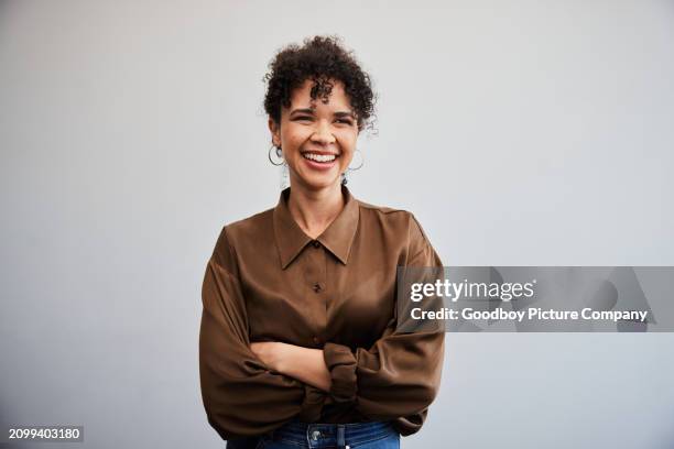 jeune femme d’affaires rieuse debout avec ses bras croisés contre un mur de bureau - portrait photos et images de collection