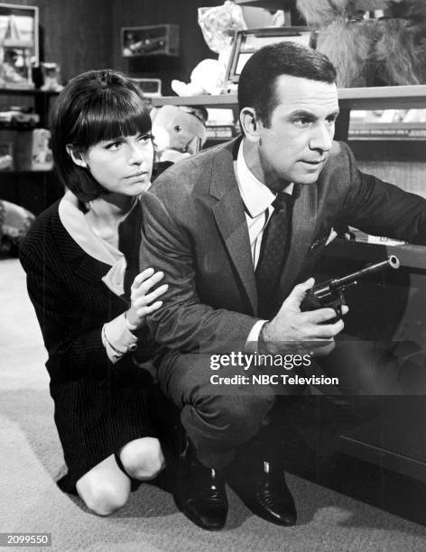 American actors Barbara Feldon and Don Adams hide behind a desk in a still from the television program, 'Get Smart,' circa 1967.