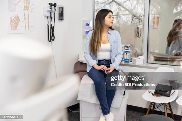 teenage girl waits patiently for doctor to return - medische onderzoekskamer stockfoto's en -beelden