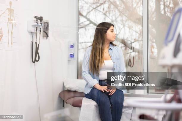 bored teen girl waits on examination table to see doctor - erbore stock pictures, royalty-free photos & images