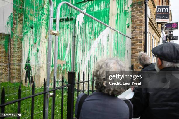 Members of the public look at a mural by the artist Banksy following it's defacement with white paint, on March 20, 2024 in the Finsbury Park area of...
