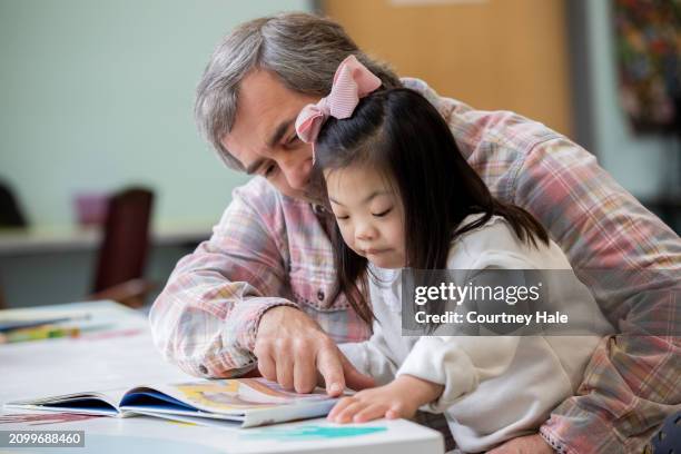 little girl with down syndrome reads picture book with her adopted father - adopted chinese daughter stock pictures, royalty-free photos & images