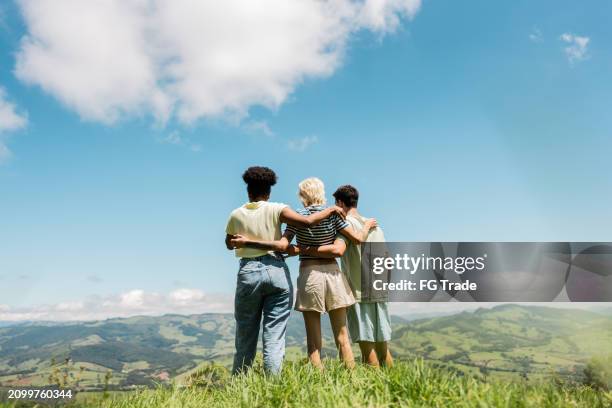 rückansicht von jungen freunden, die sich auf einem berg umarmen - arm umlegen stock-fotos und bilder