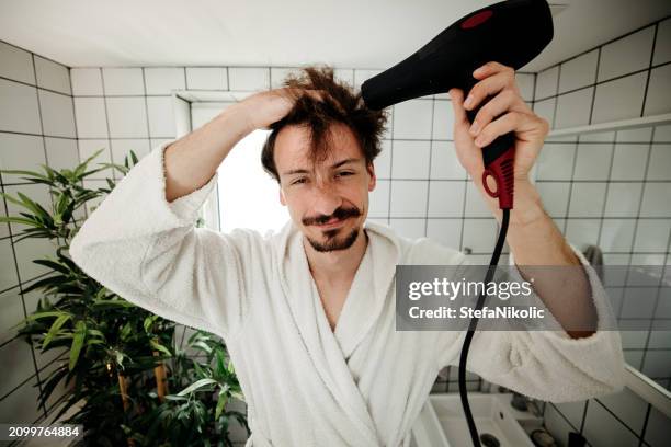 man drying his hair with a hairdryer ina bathroom - hand holding hair dryer stock pictures, royalty-free photos & images