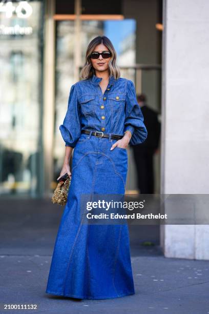 Guest wears a long blue denim dress, a black leather belt, a gold bag, sunglasses, outside Zimmermann, during the Womenswear Fall/Winter 2024/2025 as...