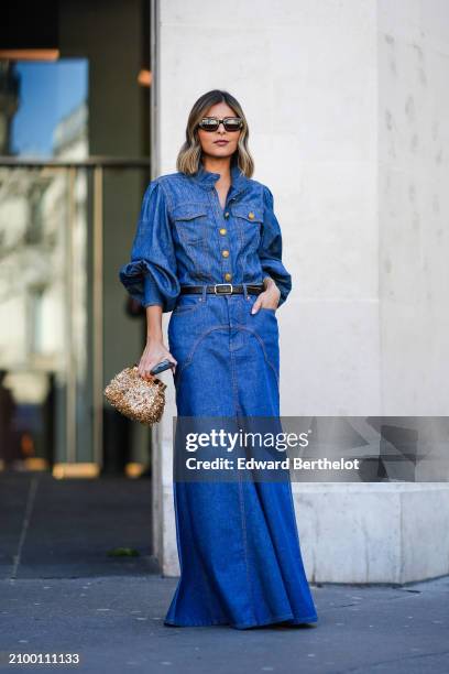Guest wears a long blue denim dress, a black leather belt, a gold bag, sunglasses, outside Zimmermann, during the Womenswear Fall/Winter 2024/2025 as...