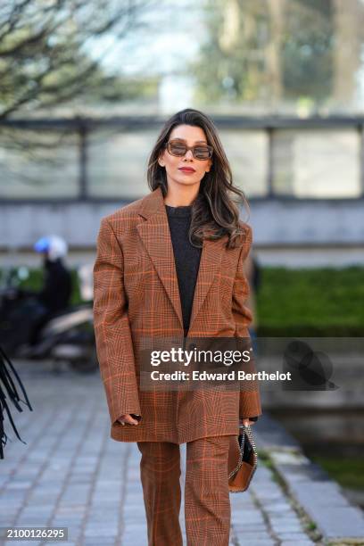 Guest wears a black top, a brown / orange checke jacket, matching pants, a brown bag sunglasses, outside Stella McCartney , during the Womenswear...