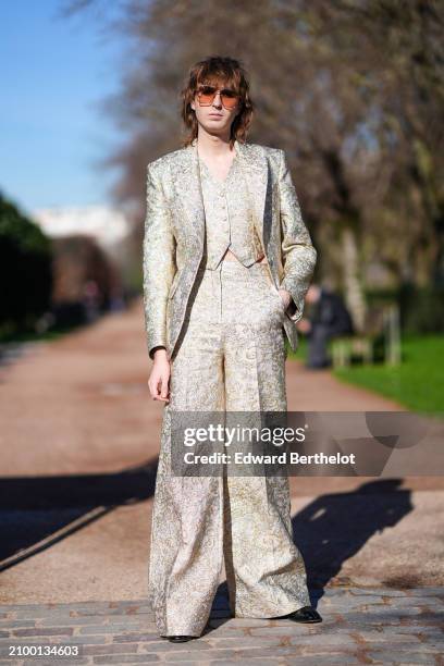 Guest wears a golden colored textured waistcoat, matching golden shiny jacket and flared pants, sunglasses, black pointed leather shoes, outside...