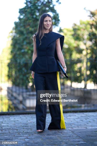 Guest wears a black top, wide-leg black and yellow pants, a black bag with gold details, outside Stella McCartney , during the Womenswear Fall/Winter...