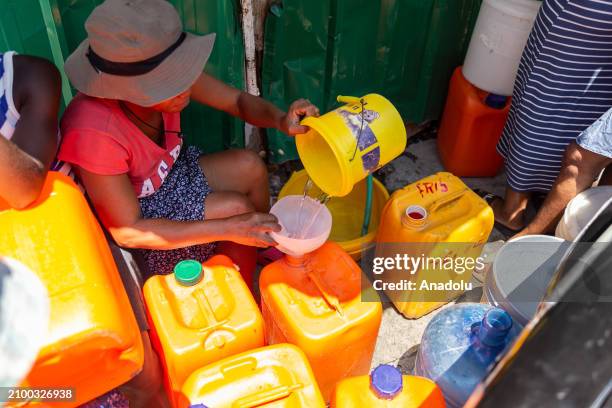 Woman fills a gallon of water with a plastic bucket on the rue de port-au-prince, against the backdrop of continuing insecurity and political...