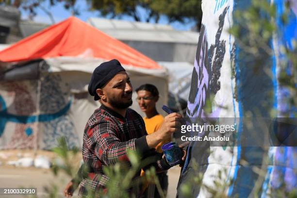 Palestinian calligraphy artist, Ayman Al-Husari, who escaped from Israeli attacks and took refuge in Rafah, draws graffities on the makeshift tents...