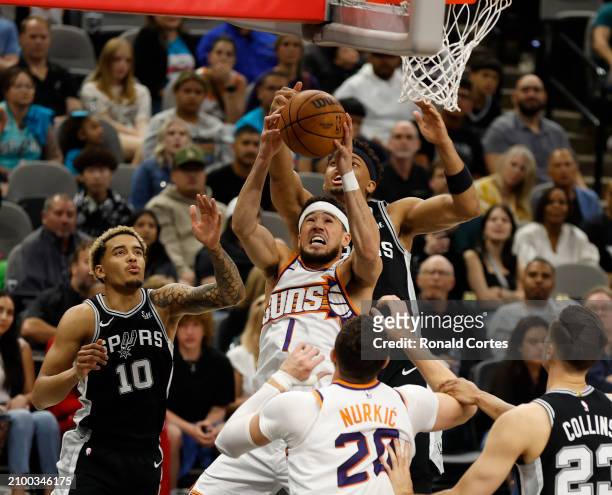 Devin Booker of the Phoenix Suns drives in front of Keldon Johnson of the San Antonio Spurs in the first half at Frost Bank Center on March 23, 2024...