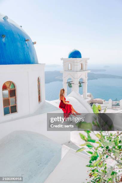 young woman enjoys traveling and looking at the view in the front of a famous traditional blue dome church on a sunny summer day in santorini island, greece thira village, greece - mediterranean-blue-roof-santorini stock pictures, royalty-free photos & images