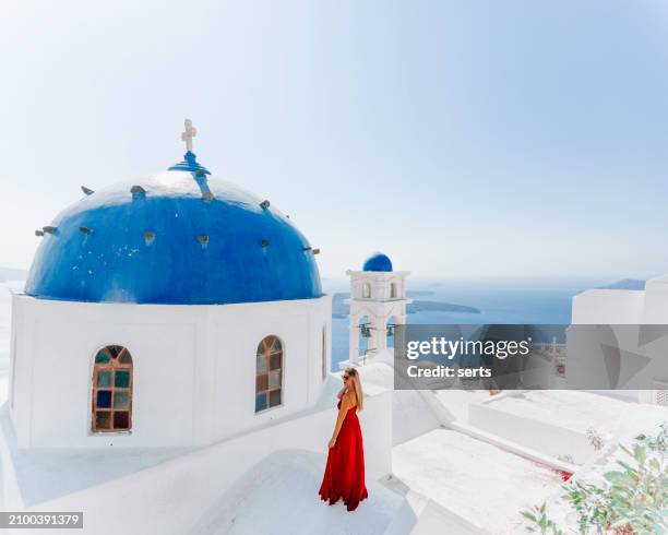 young woman enjoys traveling and looking at the view in the front of a famous traditional blue dome church on a sunny summer day in santorini island, greece thira village, greece - mediterranean-blue-roof-santorini stock pictures, royalty-free photos & images