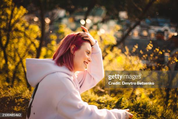 happy young woman sitting in the park during spring - 髪に手をやる　女性 ストックフォトと画像