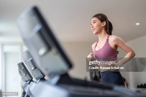 asian young sportswoman exercise by running on treadmill in gym club. attractive beautiful athlete girl practice workout to maintain muscle and burns calories for health wellbeing in fitness stadium. - cardiovasculaire training stockfoto's en -beelden