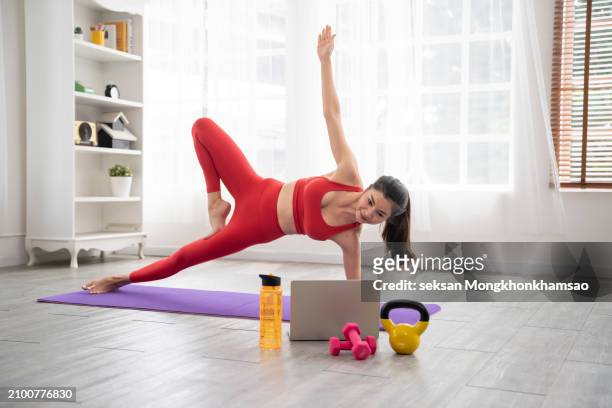 young asian woman doing online yoga class with laptop in the living room at home in the morning - flatten the curve fotografías e imágenes de stock