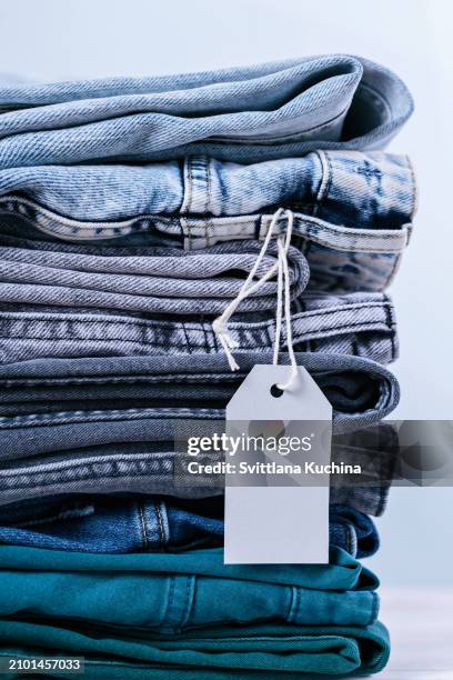 stack of blue jeans and empty tag on white background - denim pants stock pictures, royalty-free photos & images
