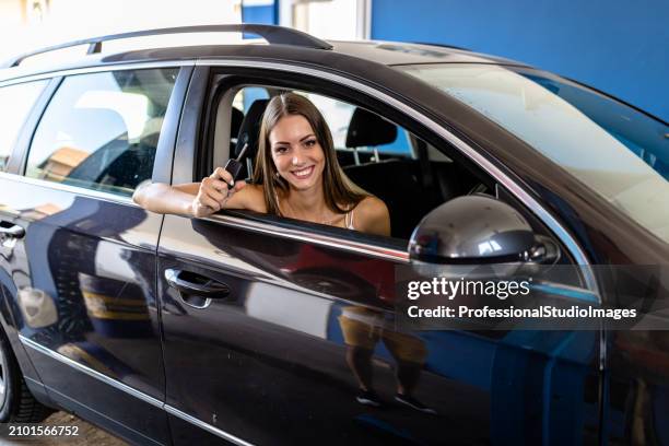 a young woman is picking up a car from the service shop and receiving a keys. - happy client by broken car stock-fotos und bilder