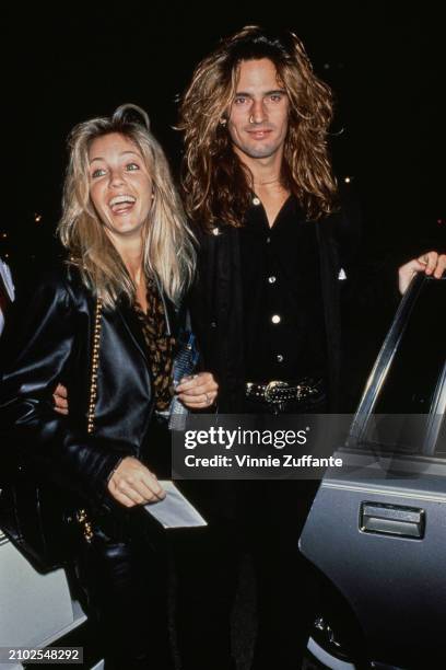 American actress Heather Locklear, wearing a black leather jacket with a gold chain shoulder strap over her right shoulder, and her husband, American...