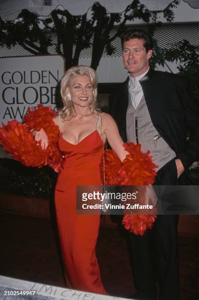 American actress Pamela Bach, wearing a red dress with a red feather boa, and her husband, American actor and singer David Hasselhoff, who wears a...